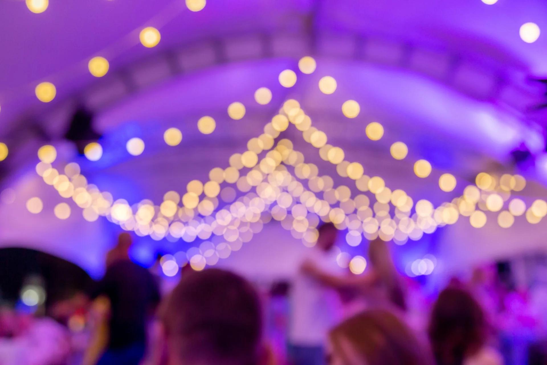 Paarse en gele verlichting boven dansende gasten op een professioneel DJ-event, illustrerend hoe juiste audiovisuele setup het feestgevoel bepaalt.