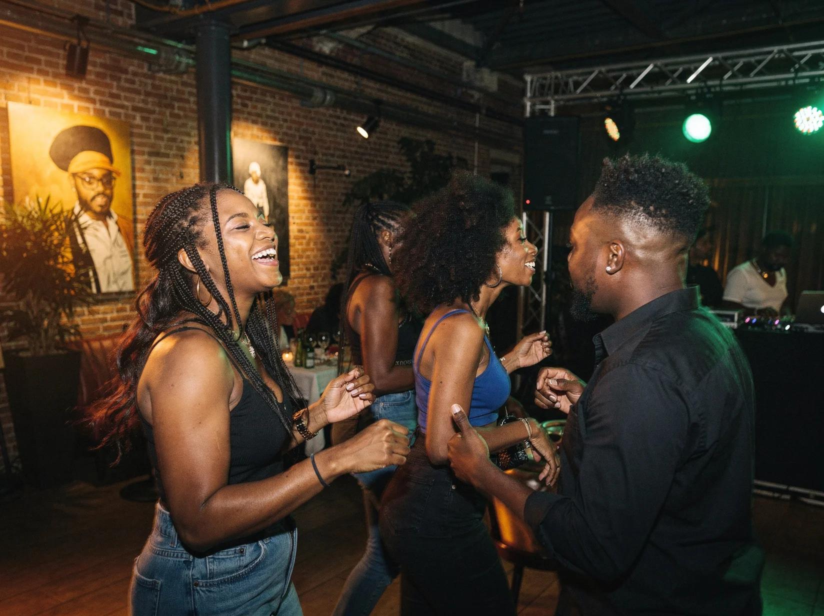 Groep vrienden danst uitgelaten op een afrobeats-DJ in een sfeervolle industriele feestlocatie