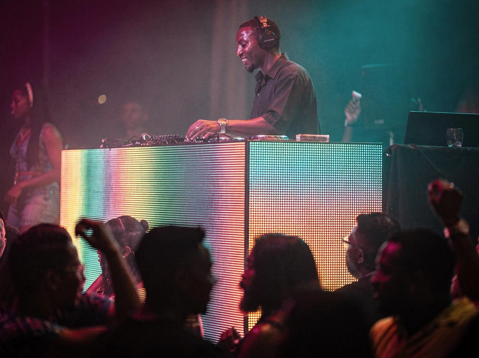 Afrobeats DJ mixing behind a glowing booth while a lively crowd dances in colourful club light