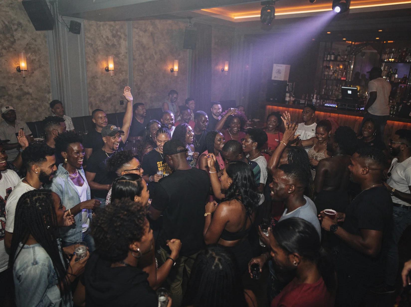 Packed dance floor at a club with an afrobeats DJ keeping the crowd moving under warm coloured lights