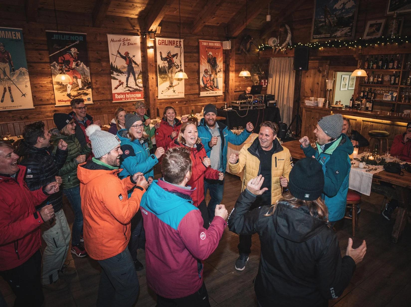 Volle zaal met gasten in skikleding die meezingen op een après-ski feest in een als hütte aangeklede feestzaal