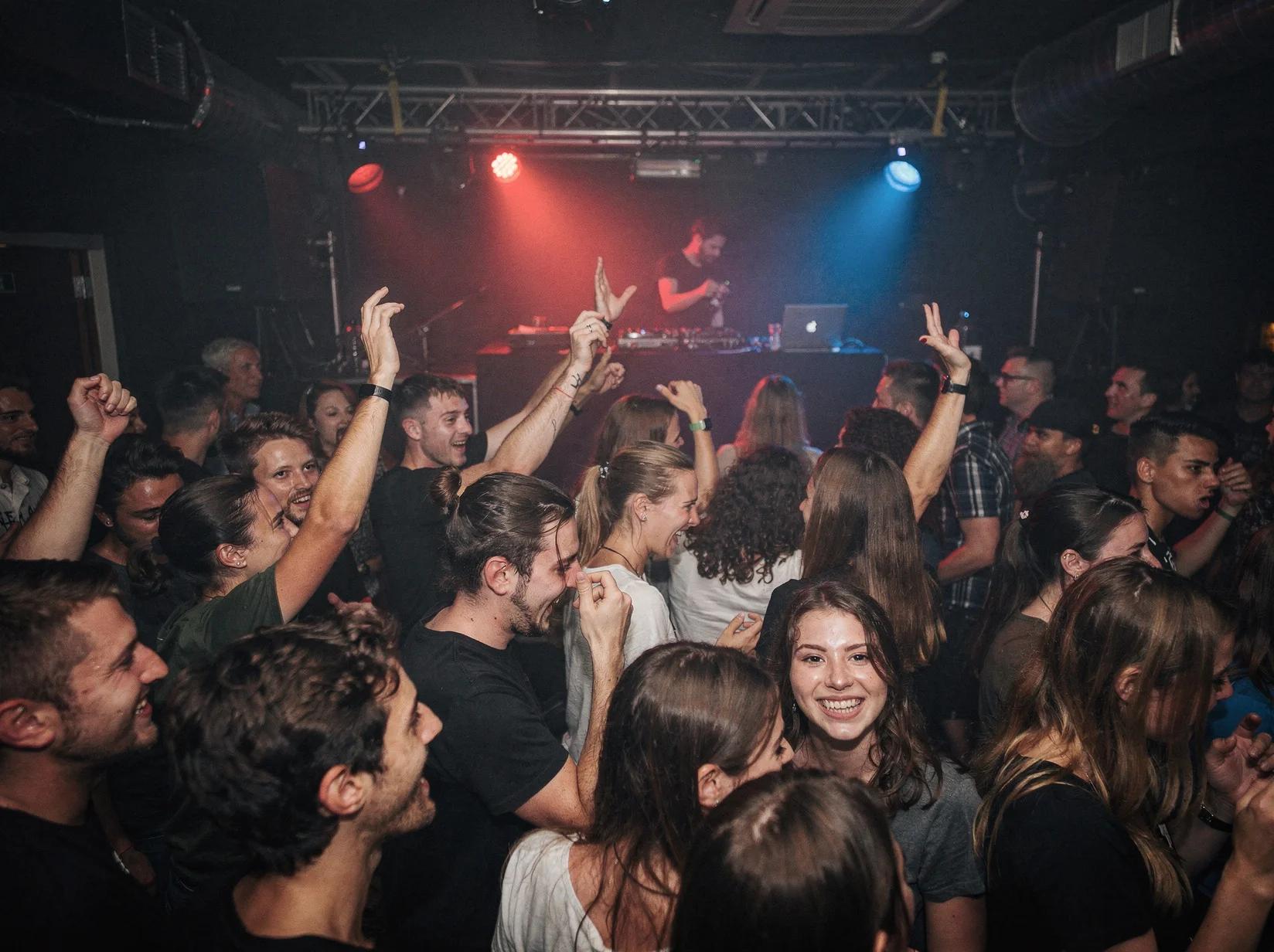Crowd dancing close together at an underground drum & bass night lit by red and blue light