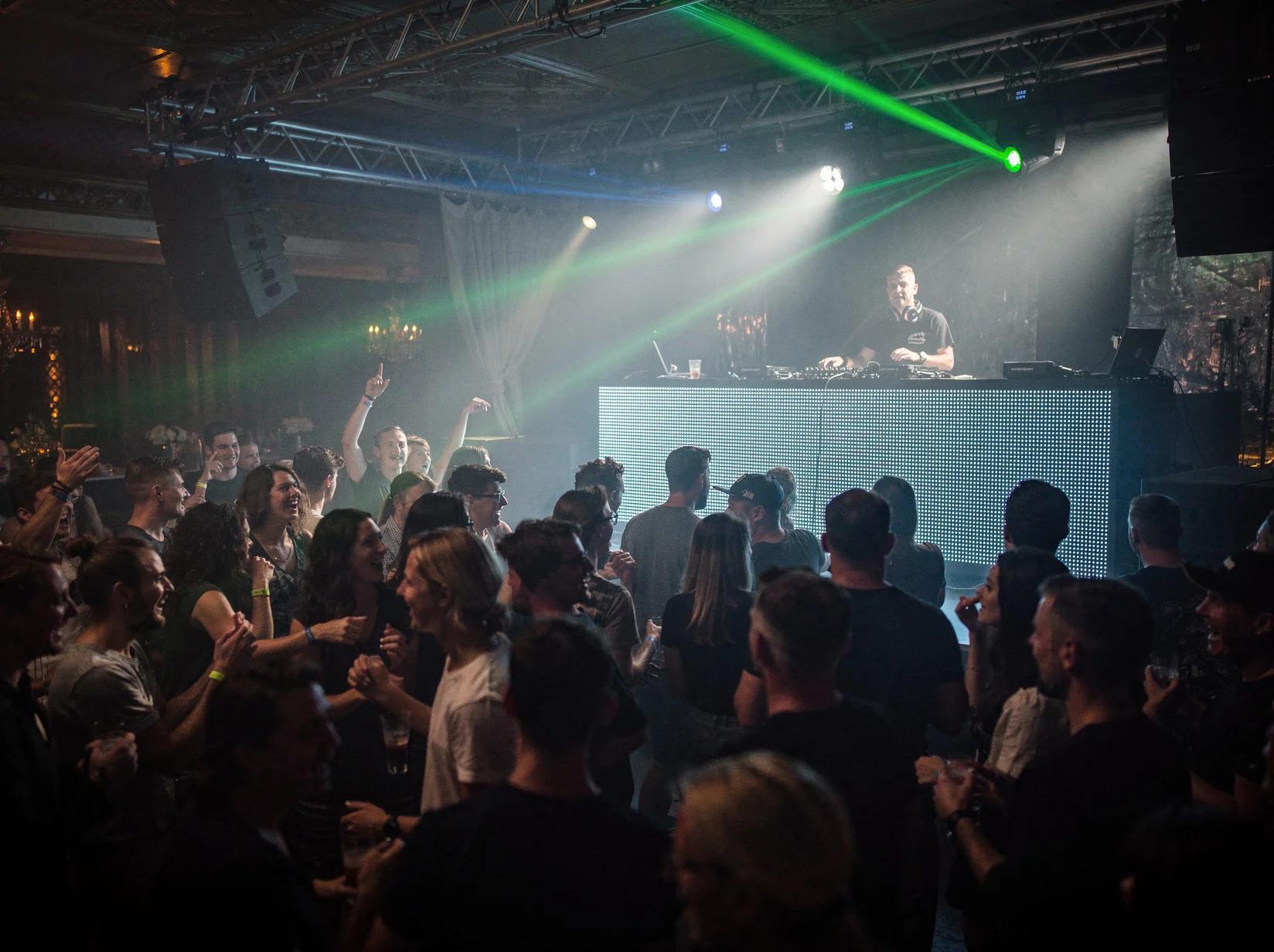 Drukke dansvloer tijdens een drum en bass-feest met een DJ achter de booth in blauwgroen licht