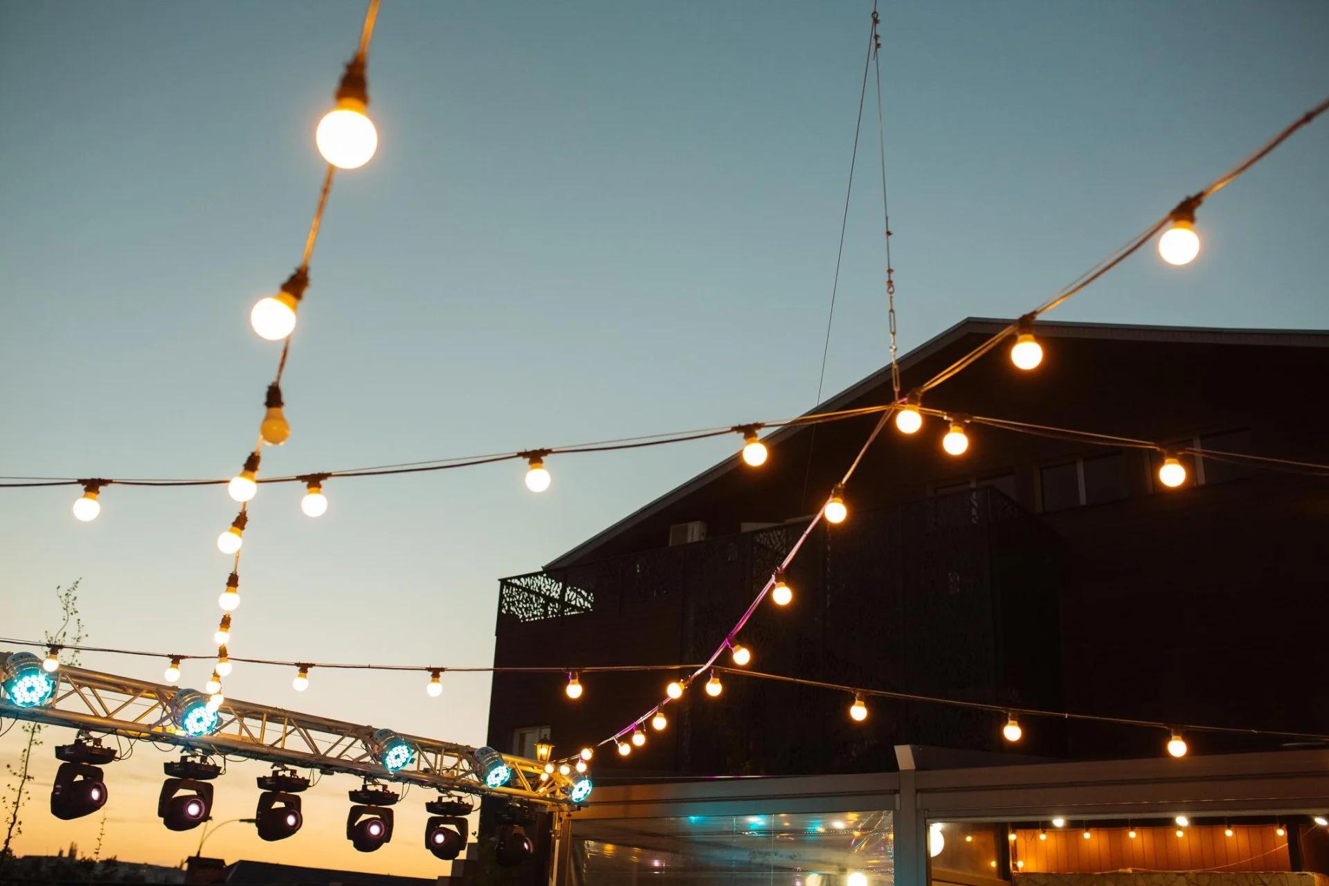 Evening setup for a corporate event with a speaker system, spotlights and atmospheric string lights above the stage.
