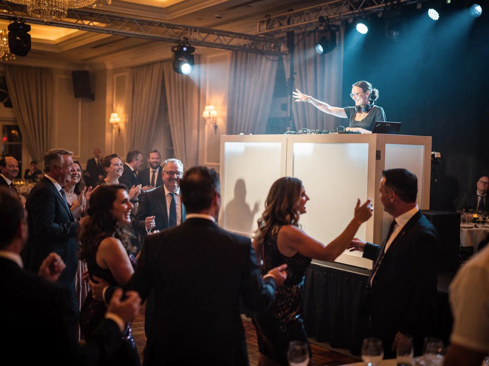 Guests in evening wear dancing while a gala DJ mixes behind a sleek booth in an elegant ballroom