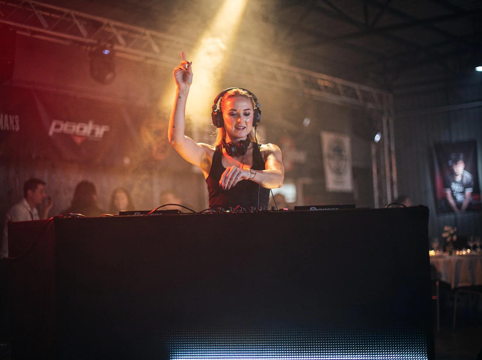 Hardstyle-DJ achter de booth met koptelefoon terwijl ze het publiek op een warehouse-feest aanstuurt