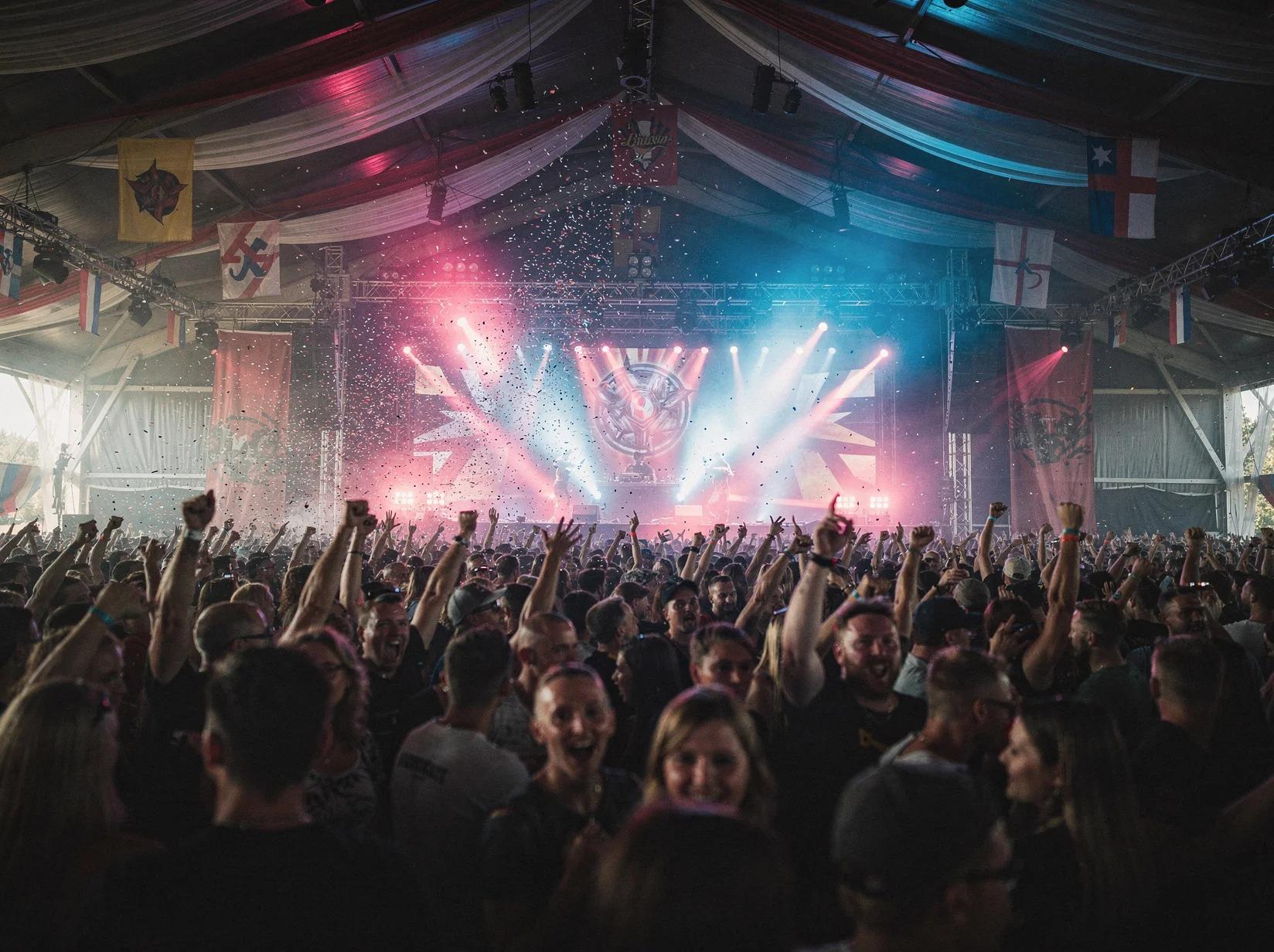 Volle feesttent met een uitzinnige menigte die danst voor een hardstyle-DJ onder gekleurde spots