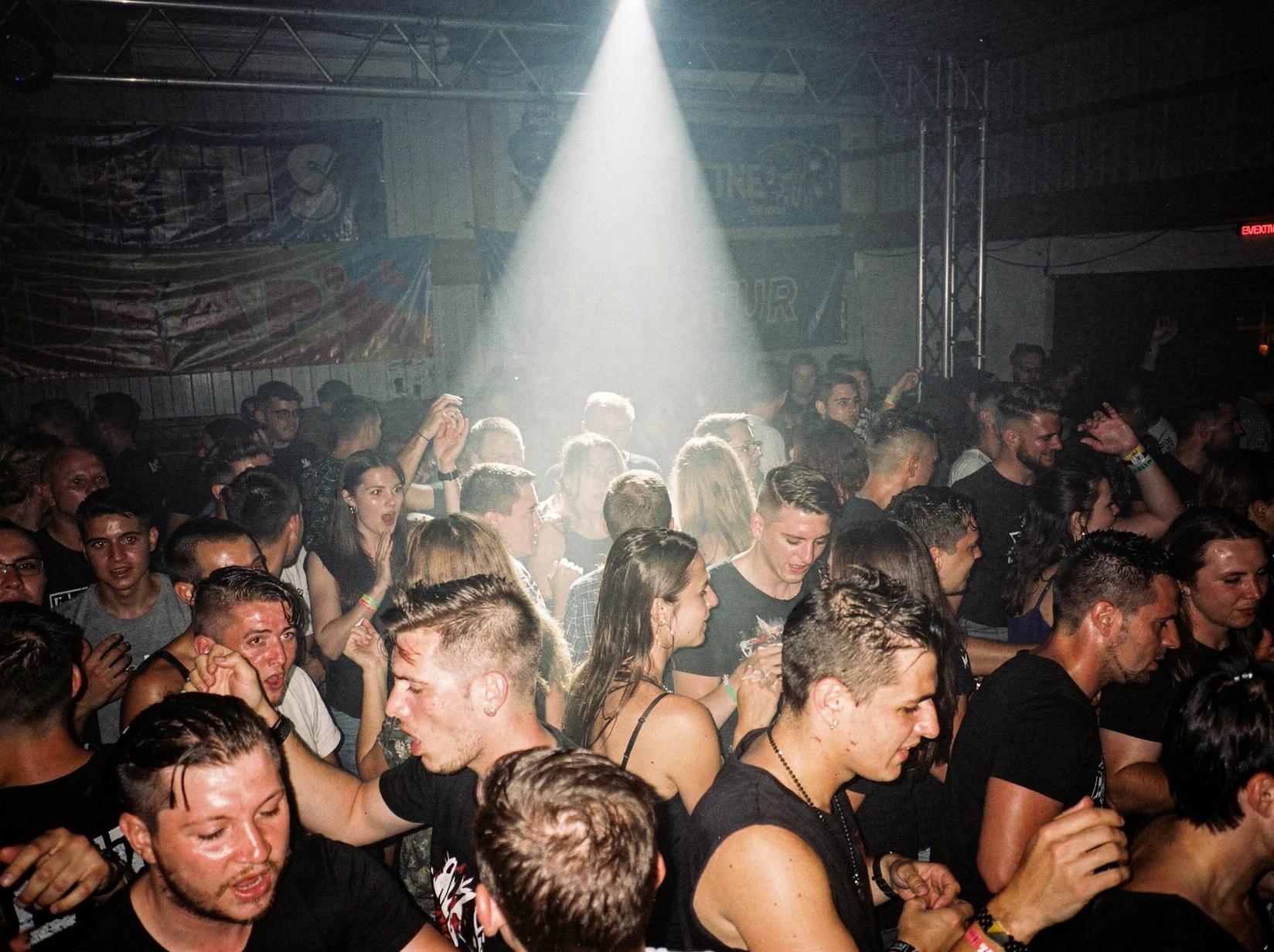 Donker warehouse-feest waar het publiek intens danst op de keiharde kick van een rawstyle-DJ