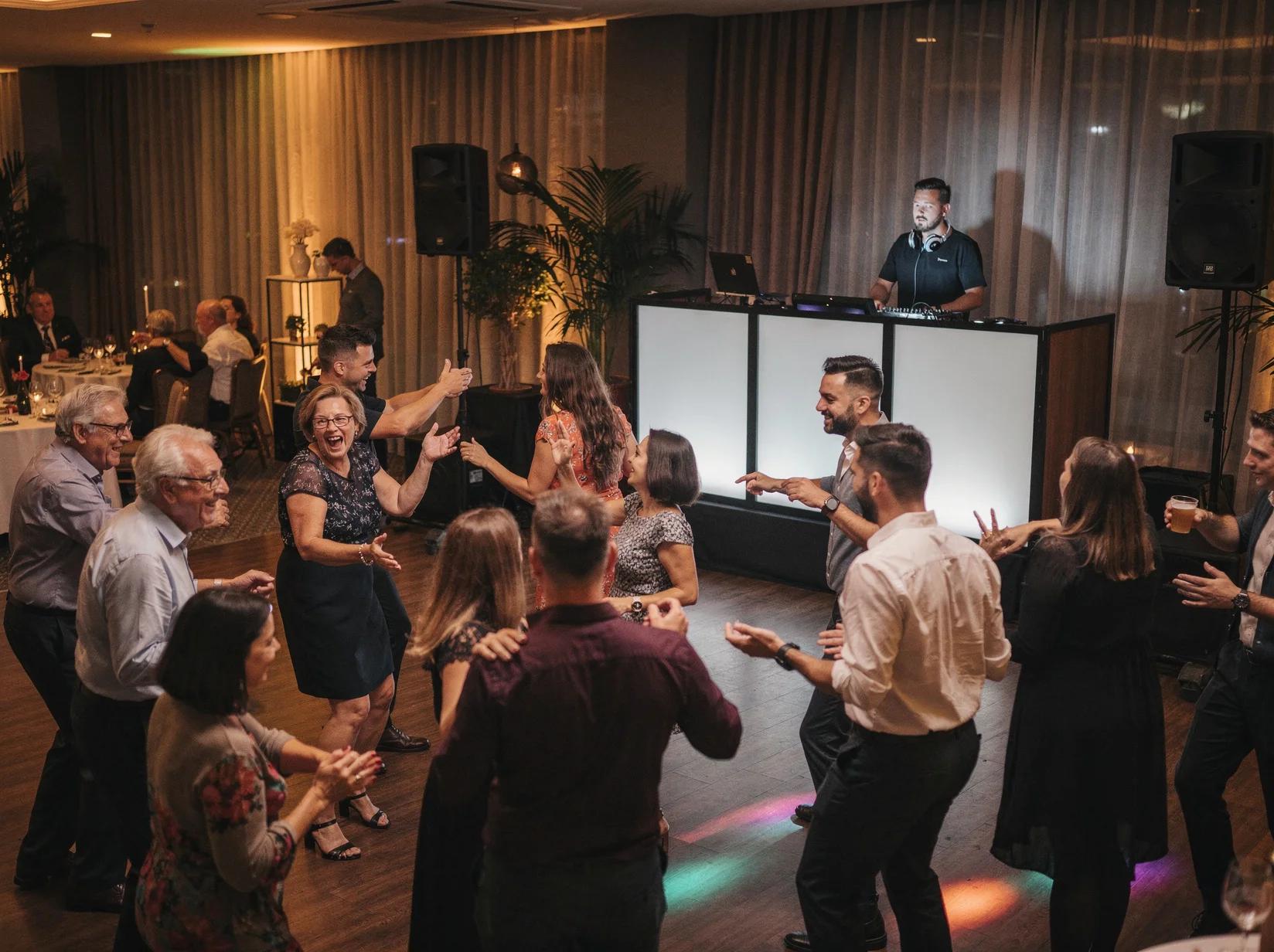 Gasten van verschillende generaties dansen samen op een jubileumfeest terwijl de jubileum DJ op de achtergrond draait