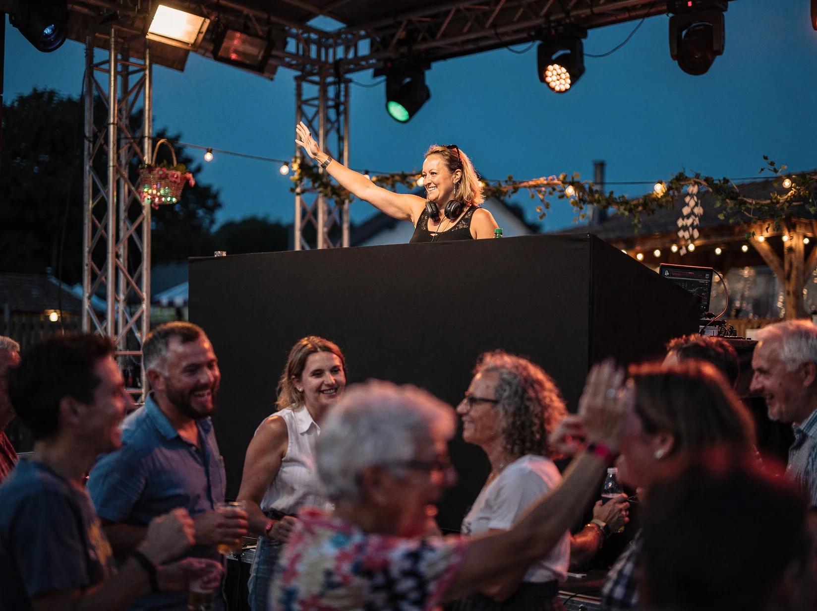 DJ achter een podium op de kermis die een gemengd publiek van jong tot oud laat dansen tijdens het dorpsfeest