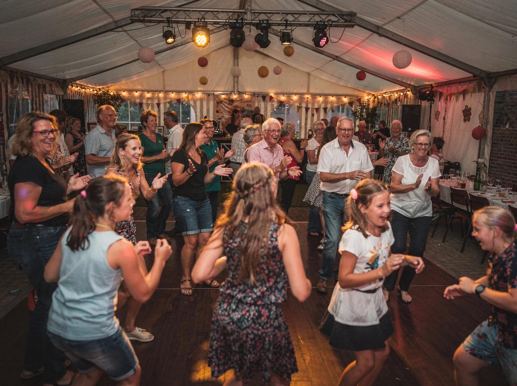 Breed gemengd publiek dat danst in een feesttent op het dorpsplein tijdens een dorpsfeest met een DJ
