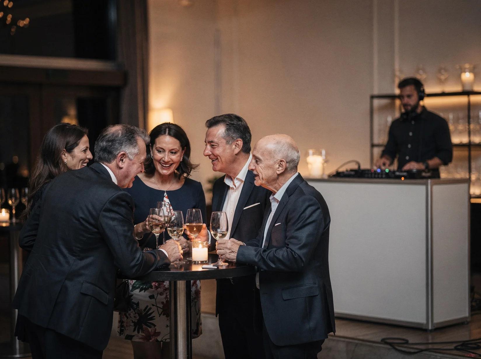Guests talking closely at a reception while a lounge DJ reads the room from the booth