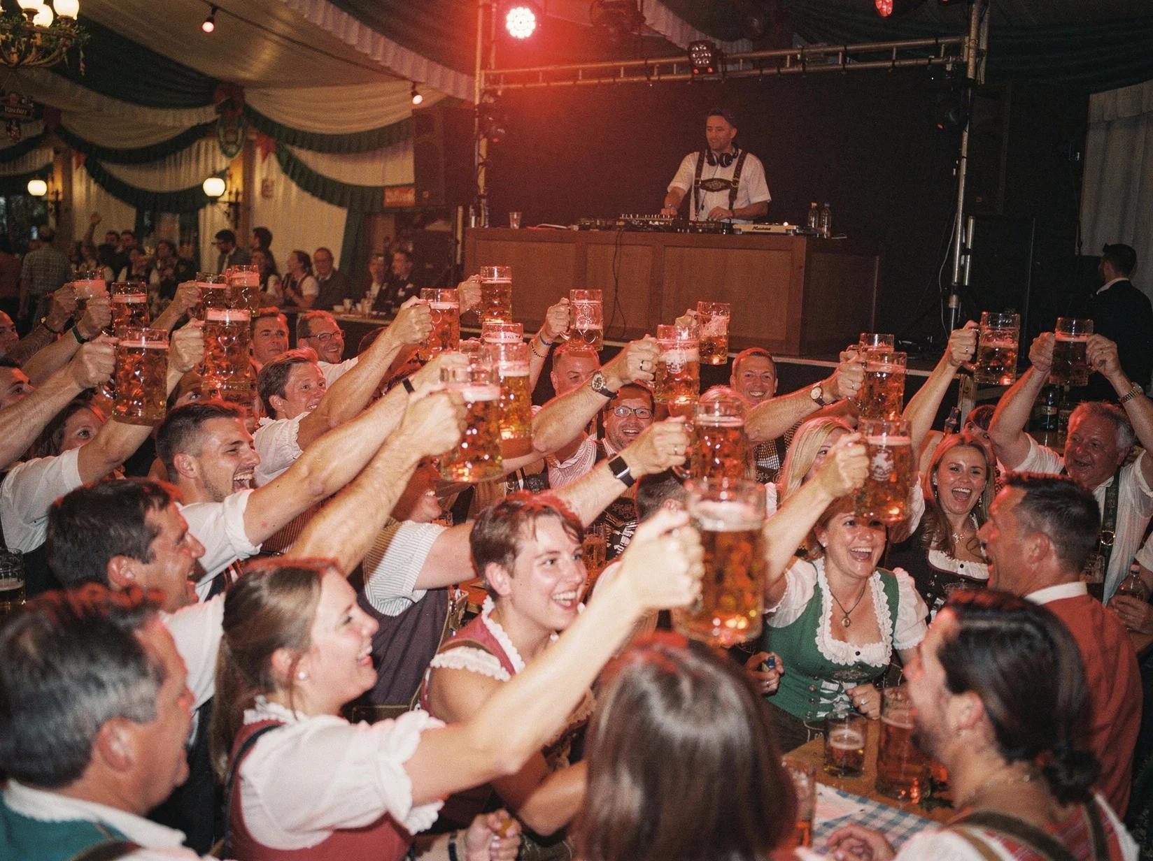 Beer tent guests raising steins during a singalong anthem as the Oktoberfest DJ keeps the energy high
