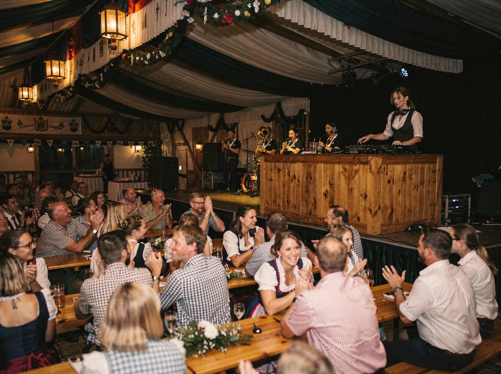 Guests dancing in a traditional beer tent beside a brass band and Oktoberfest DJ at a local festival