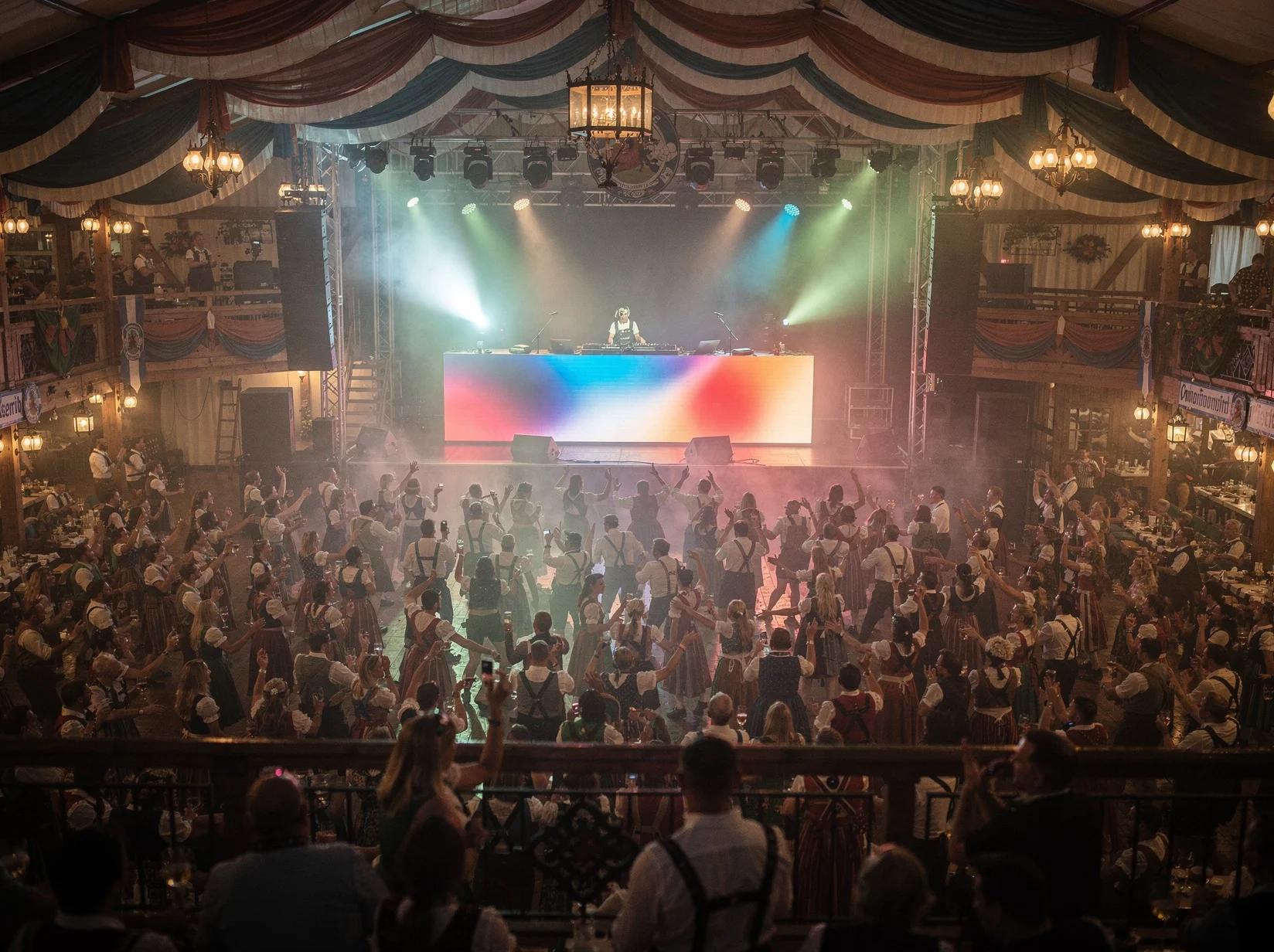 Massive crowd dancing in a festival marquee with a stage and Oktoberfest DJ at a large beer festival