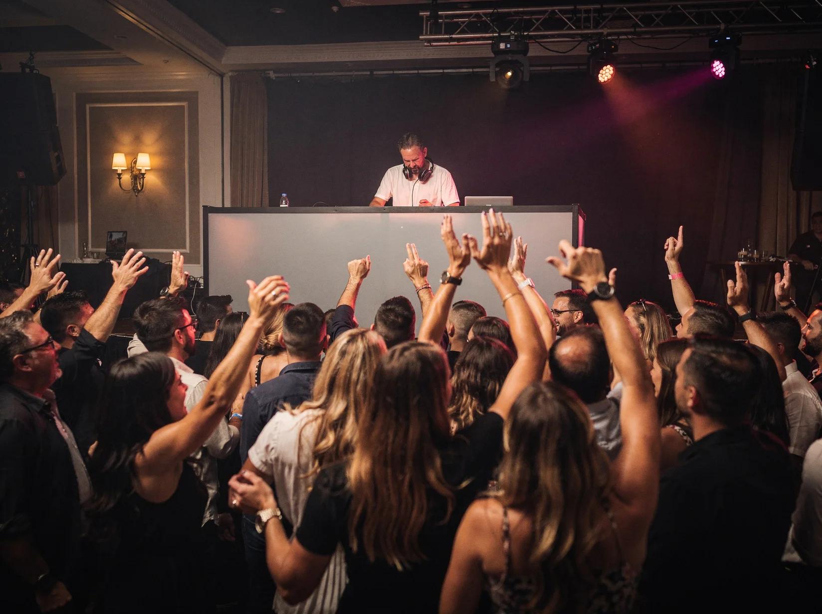 A party DJ reads the room behind the booth while the crowd keeps the energy up on the dance floor