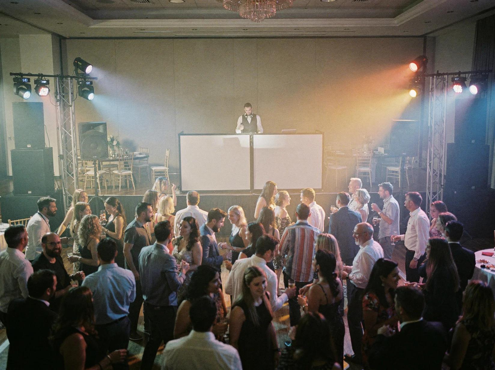 A party DJ set up with a full sound and light rig in a large hall while a hundred guests fill the dance floor
