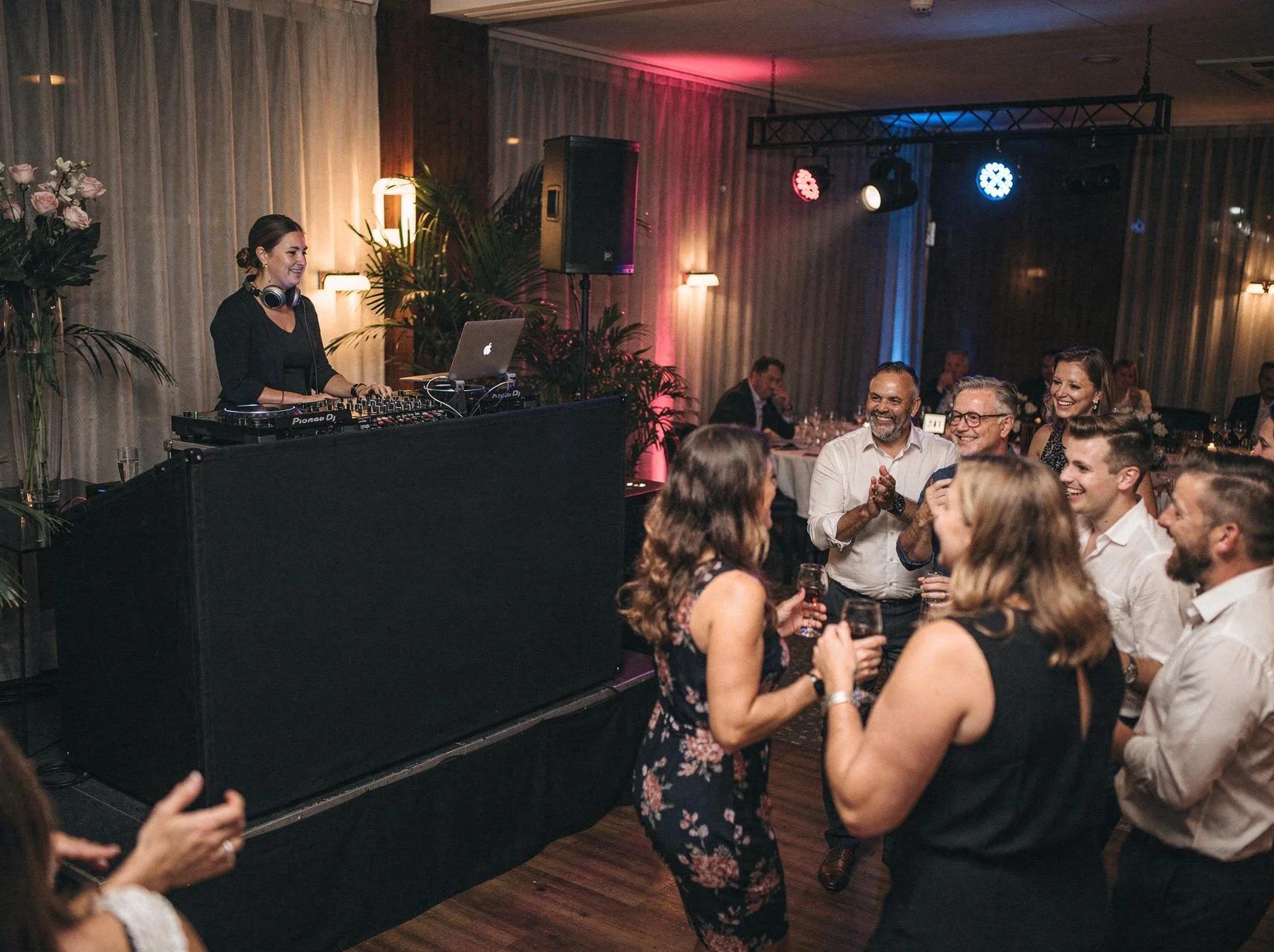 Een DJ voor jouw privéfeest achter de booth terwijl een kleine groep gasten uitgelaten danst in een sfeervolle gehuurde zaal