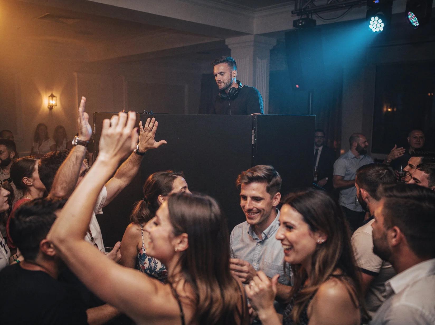 A professional DJ behind the booth guiding a lively crowd through the night at a real party venue