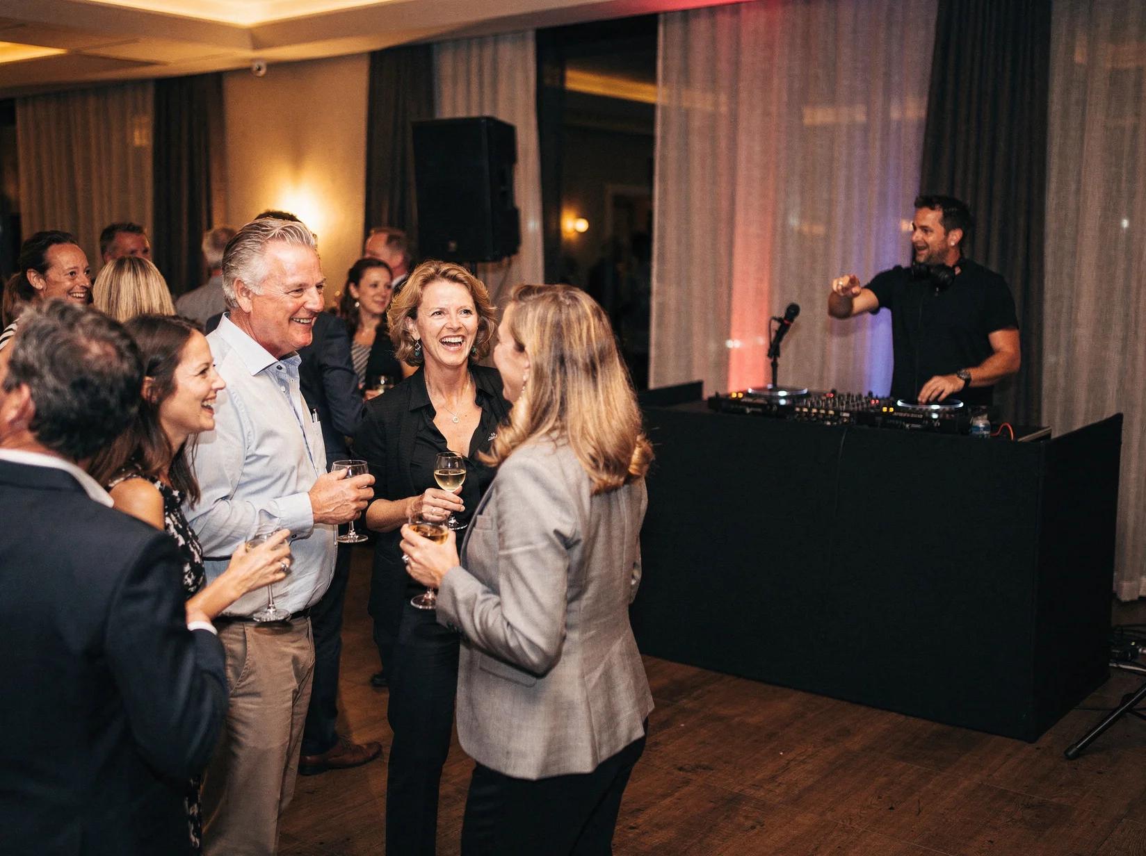 Gasten die gezellig met elkaar praten tijdens een receptie met een DJ die subtiele sfeermuziek draait op de achtergrond