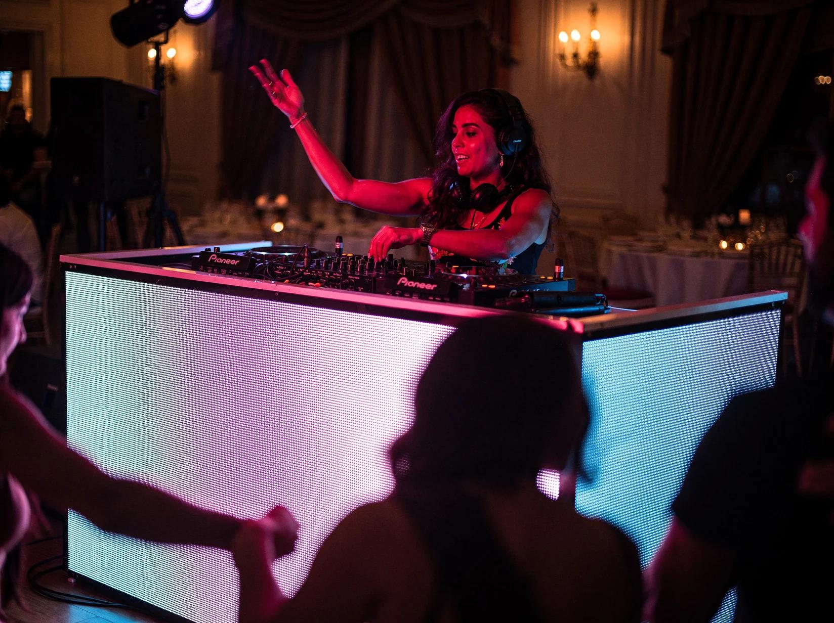 Reggaeton DJ mixing behind a glowing booth while the crowd dances in a club