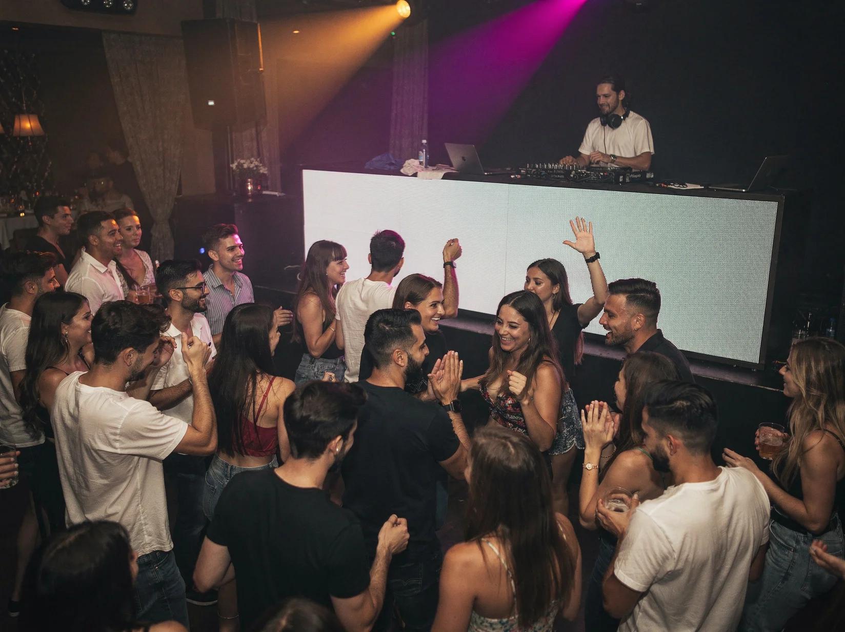 Volle dansvloer met jong publiek dat danst terwijl een reggaeton-DJ de set draait in een sfeervol verlichte club