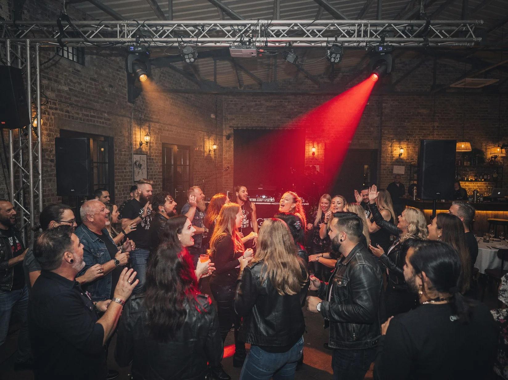 Volle feestzaal waar een publiek meezingt met de rock-DJ tussen warme spots en rookwolken
