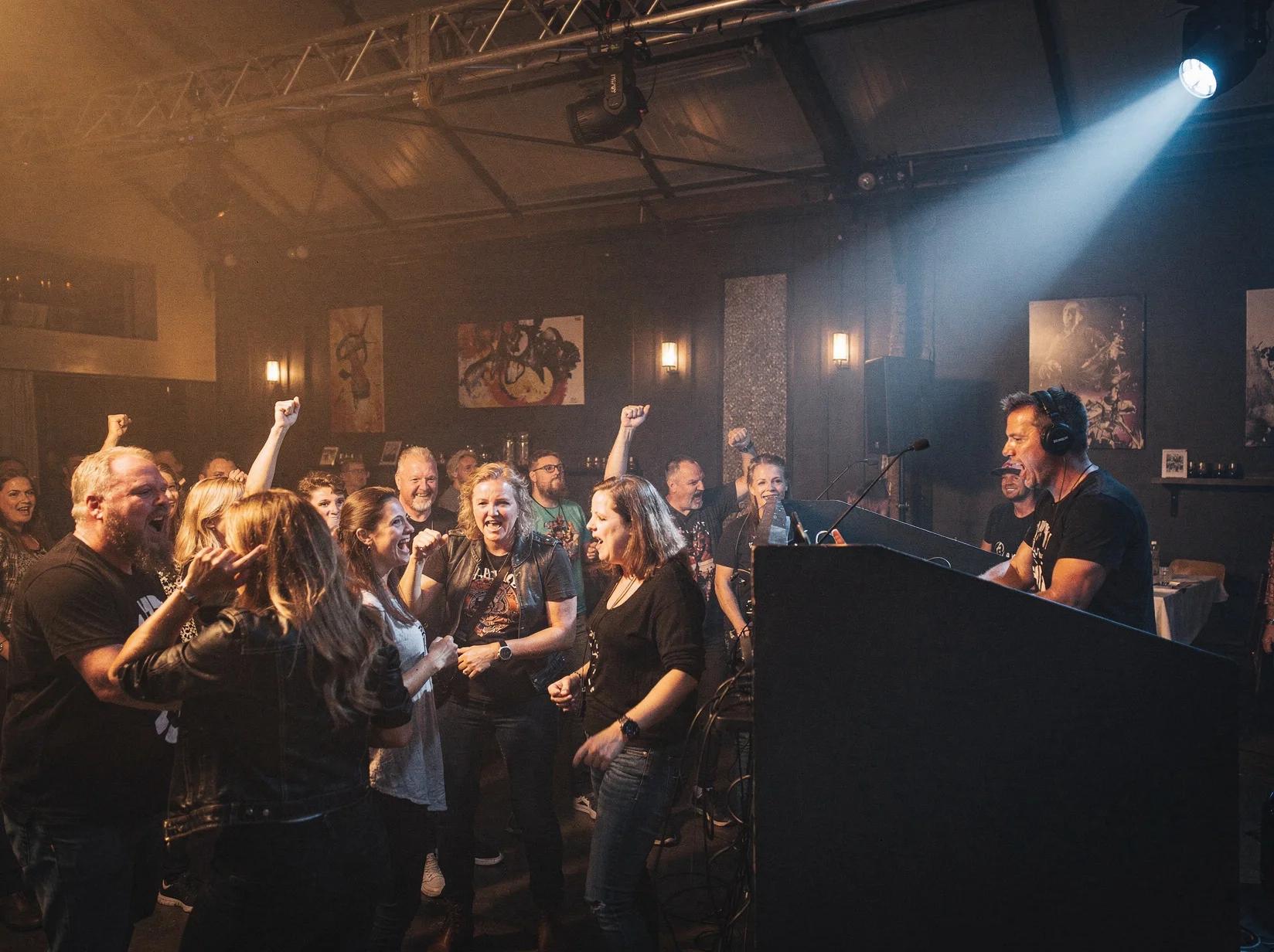 Crowd singing and dancing to a rock DJ in a dim industrial event hall
