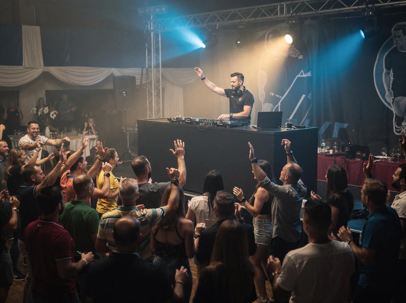 DJ op een podium die het publiek aanjaagt tijdens een sportevenement in een feestelijk aangeklede sporthal