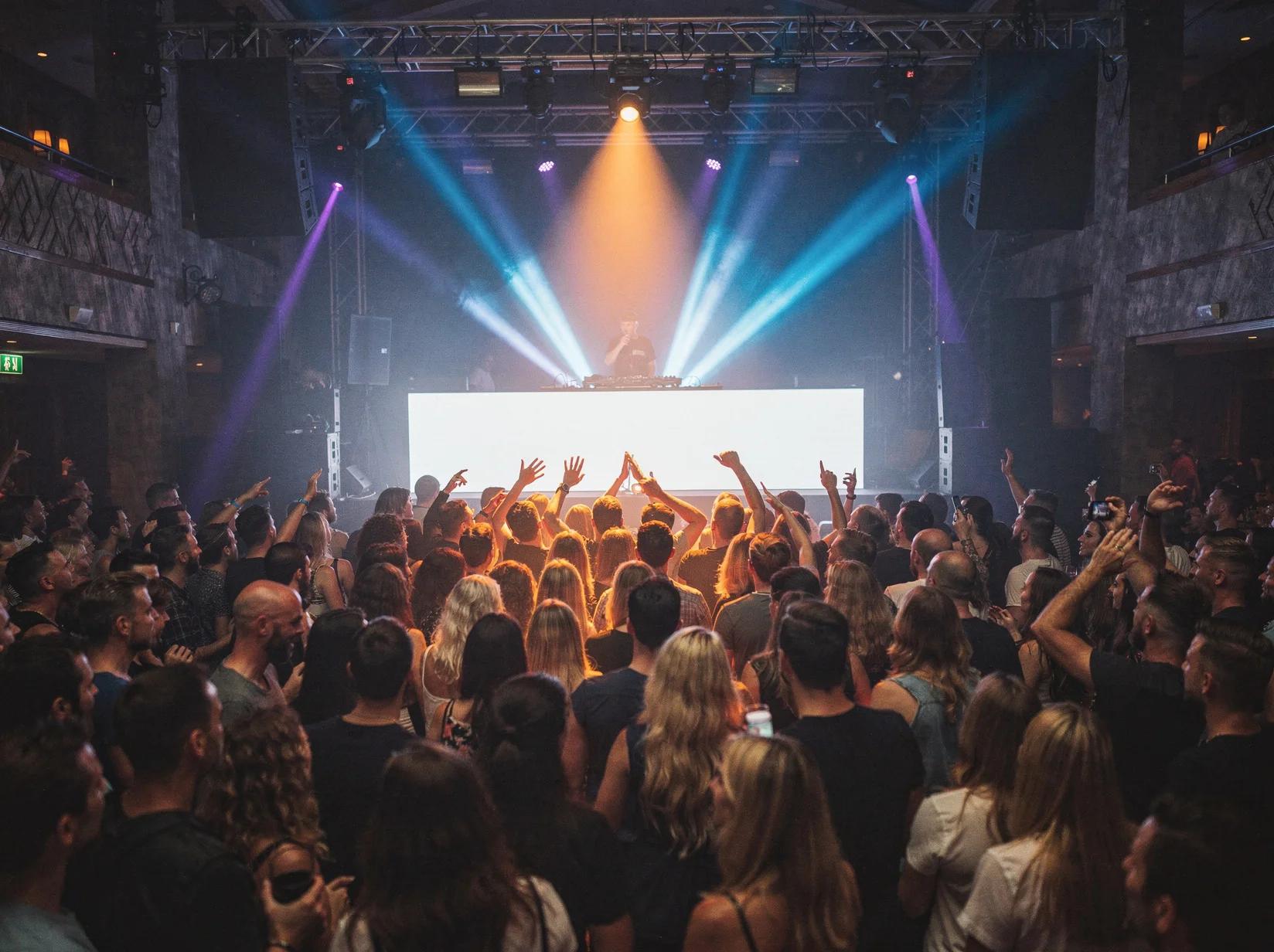 Packed club dance floor in full swing as a trance DJ holds the energy from the booth
