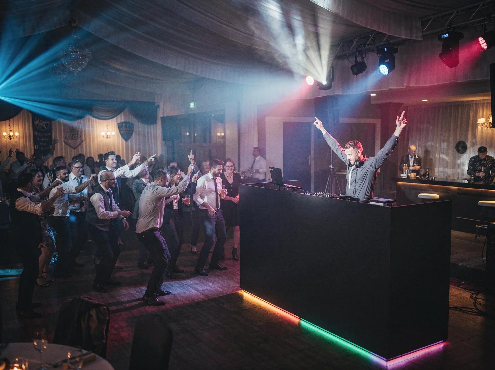 Volle dansvloer met tientallen gasten en een DJ achter een strakke booth in een gehuurde zaal met volledige licht- en geluidsset